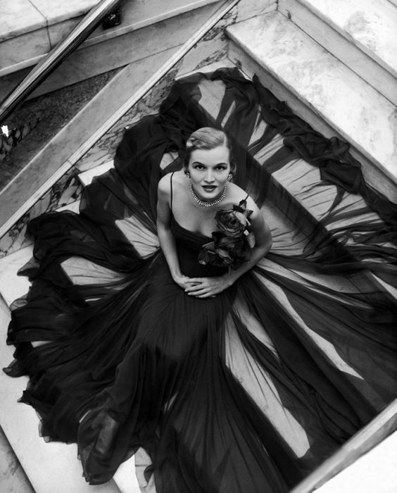 Fotografía de Nina Leen donde aparece una mujer de los años 50 0 60 sentada en una escalera con un vestido de gala 