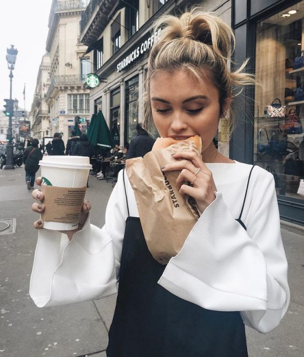 Chica comiendo un pan y café de starbucks