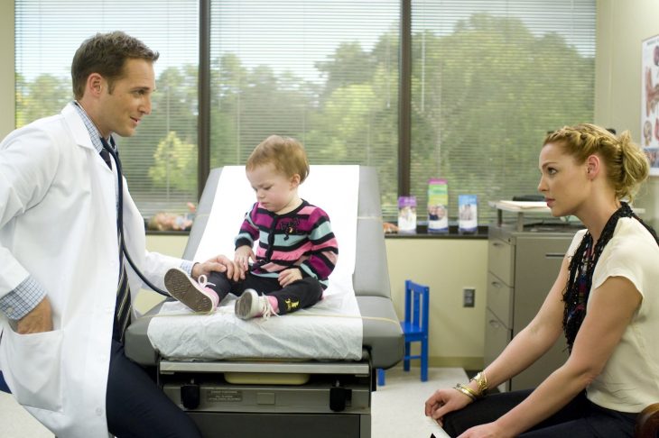 doctor en consultorio bebe sentado y mujer rubia mirando seriamente 