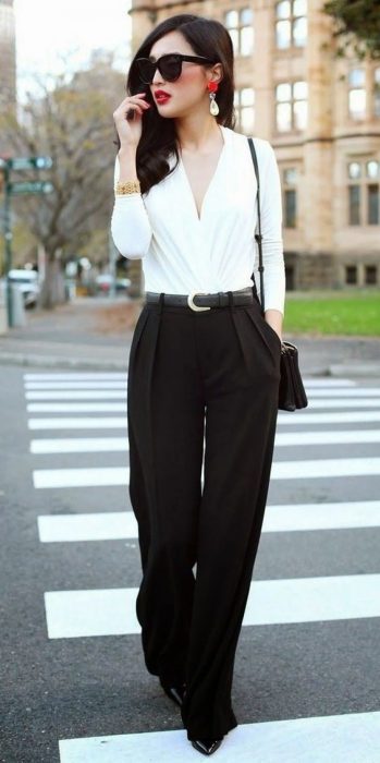 Chica usando un pantalón de color negro con una blusa de color blanco parada en medio de la calle 