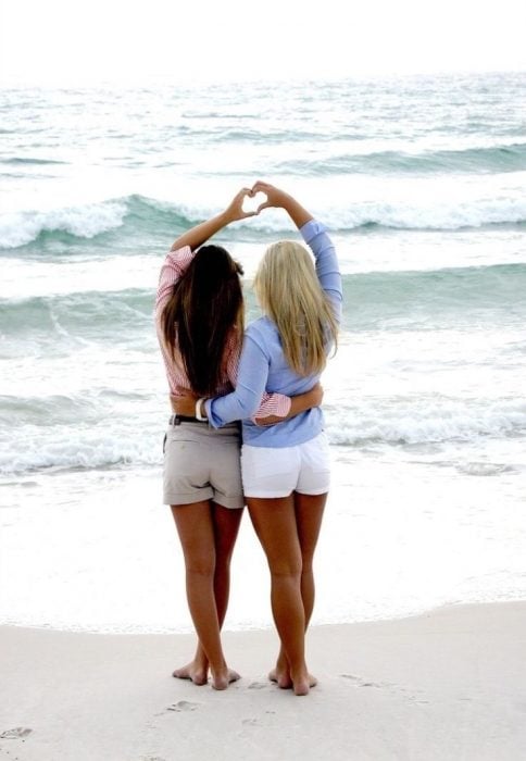 Chicas haciendo un corazón con sus manos frente a la playa 