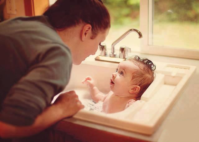 Mamá dandole un baño a su bebé en el lavabo de la cocina 