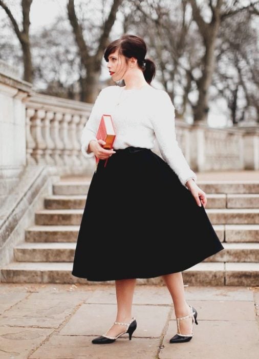 Chica parada bajo unos escalones usando falda negra, blusa blanca y tacones de 6 centímetros 