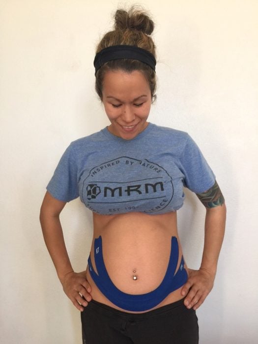 Chica con una icinta kinestape colocada sobre su vientre de embarazo 