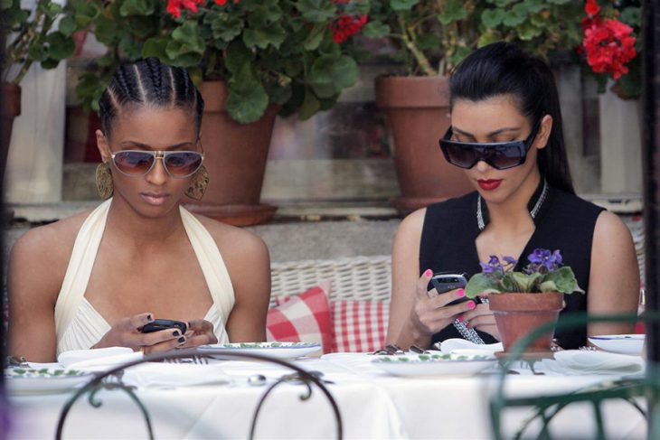 par de mujeres sentadas en una mesa usando sus teléfonos celulares 