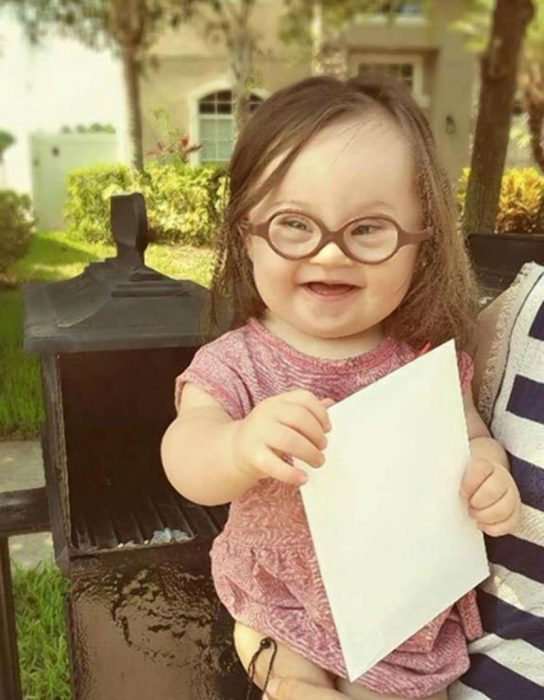 niña en brazos con lentes y carta en un buzón