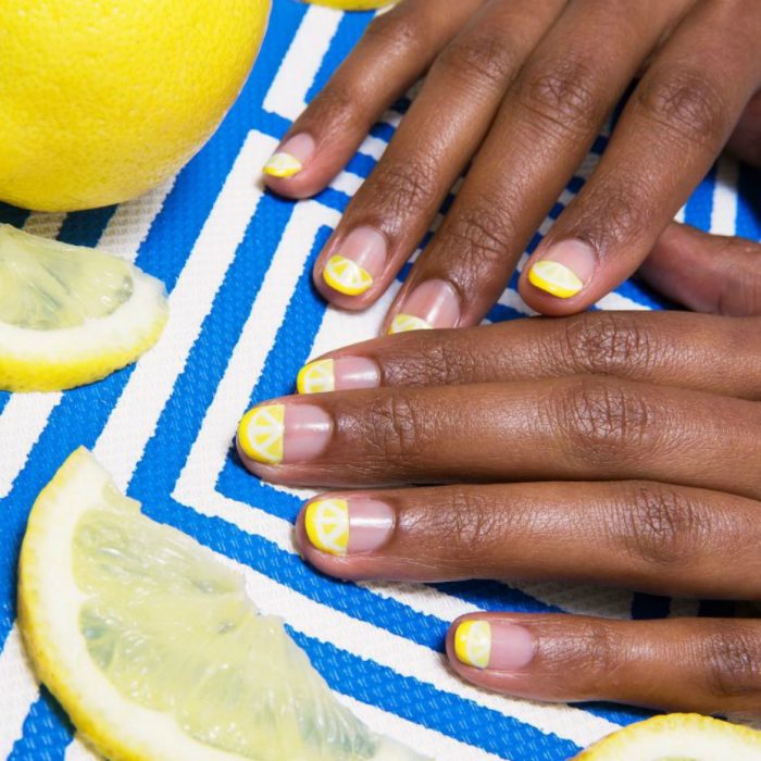 manos de mujer morena con uñas amarillas de limones 