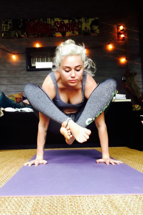 mujer rubia haciendo yoga tapete morado y luces pared 