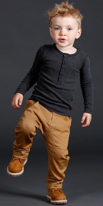 Niño mini fashionista vestido con un pantalón color café, camisa gris y botas timberland 