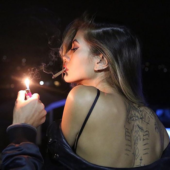 mujer de cabello rubio de espaldas prendiendo un cigarro 