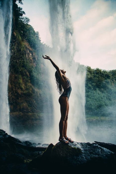 Chica levantando los brazos mientras está frente a una cascada 