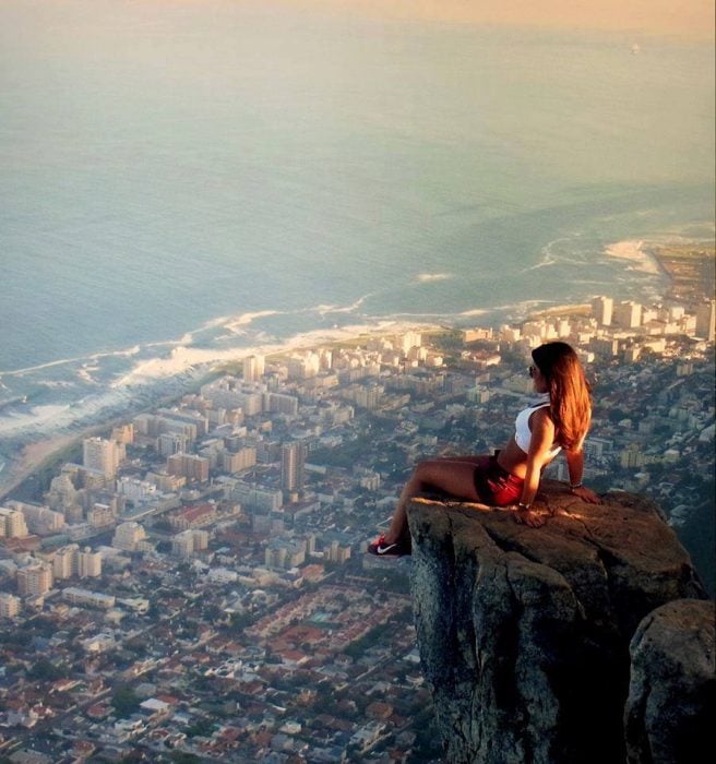 Chica sentada sobre una roca admirando una ciudad 