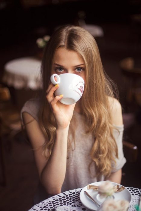 Chica sentada en una mesa bebiendo de una taza 