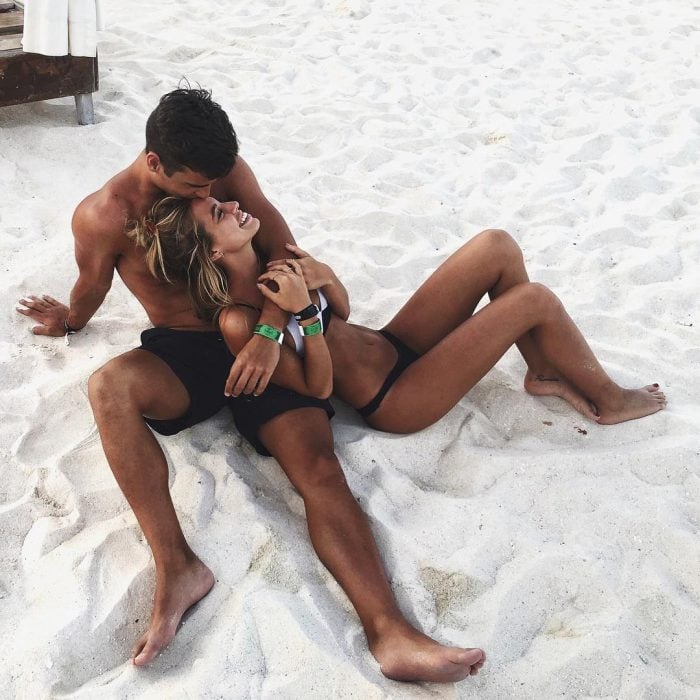 Pareja de novios recostados en la arena de la playa besándose 