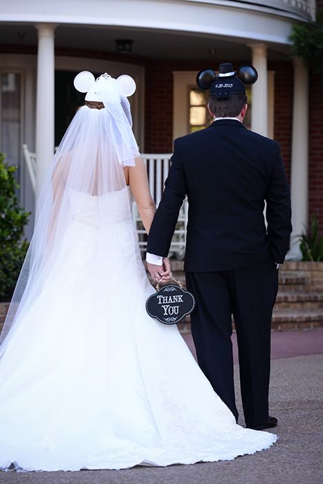 Pareja de novios con orejas de mickey mouse sosteniendo un letrero de agradecimiento 