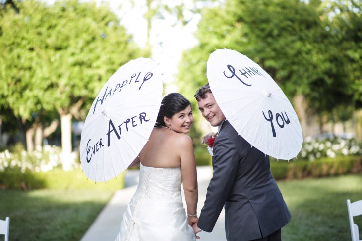 Pareja de novios sosteniendo sombrillas que dicen vivieron felices por siempre 