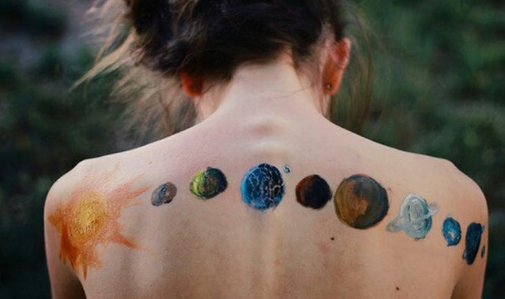 espalda desnuda de mujer con pintura de sol y planetas 