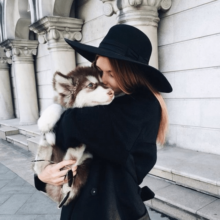 mujer de cabello castaño con sombrero negro abrazando a perro 