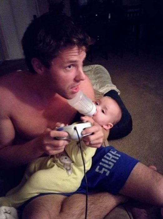 hombre jugando videojuego y dando biberón a bebé