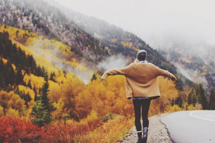 mujer abriendo sus brazos en paisaje de bosques y montañas 