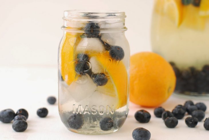 Agua de naranja y arándano con hielos servido en un vaso con agua 