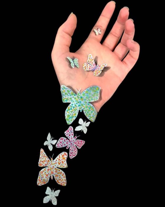 Chica que crea ilusiones ópticas en su mano con mariposas dibujadas en su brazo 