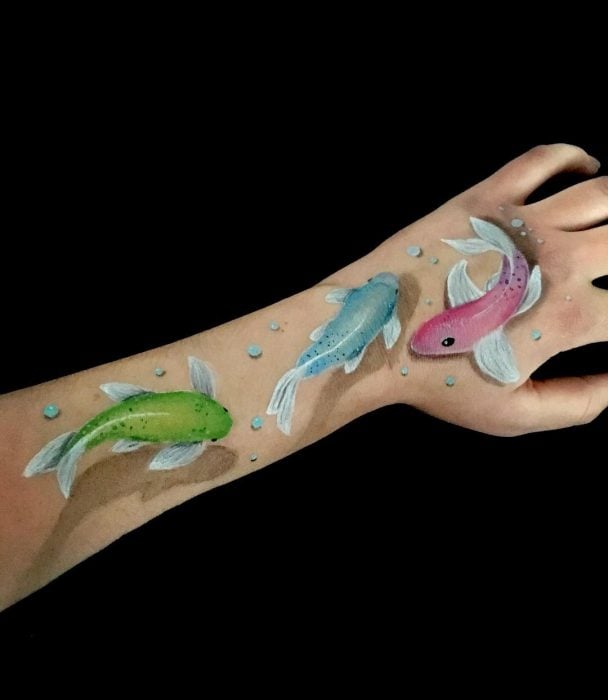 Chica que crea ilusiones ópticas en su mano, con peces coi dibujados sobre su brazo 