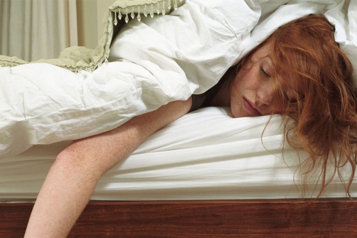 mujer pelirroja abajo de cobijas dormida en la cama 