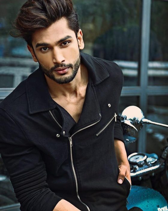 Rohit Khandelwal nuevo Mr. World usando una chaqueta negra mientras está recargado sobre una motocicleta 