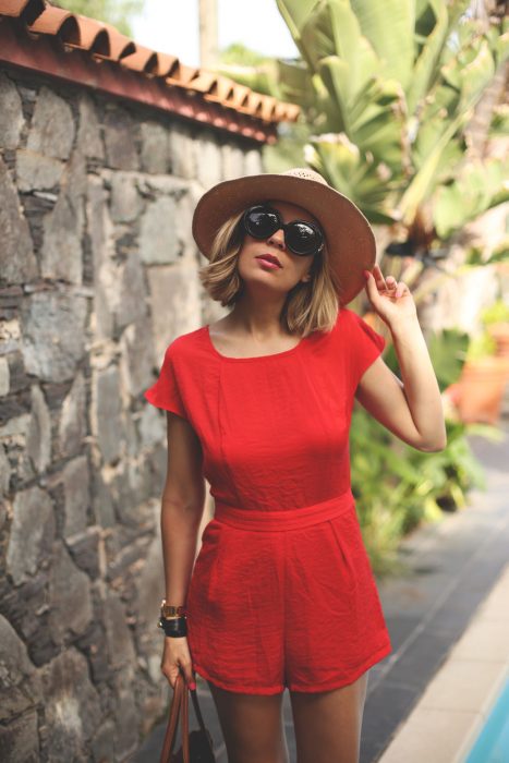 Chica usando un romper en color rojo y complementándolo con lentes y sombrero