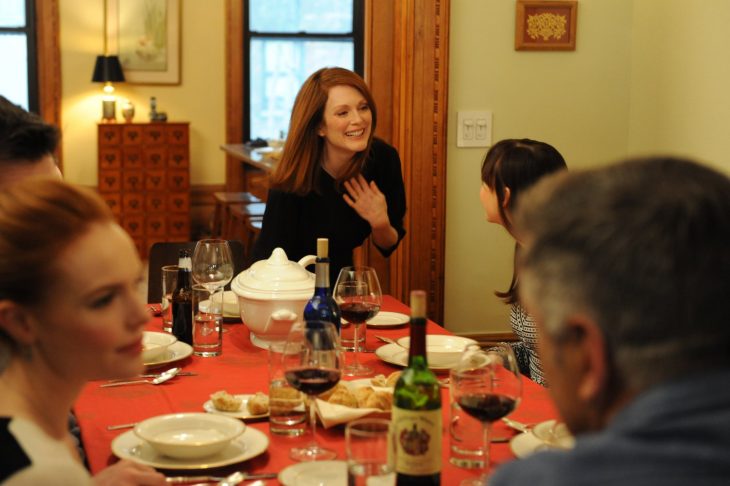 mujer cabello pelirrojo sonriendo en una mesa con copas de vino 