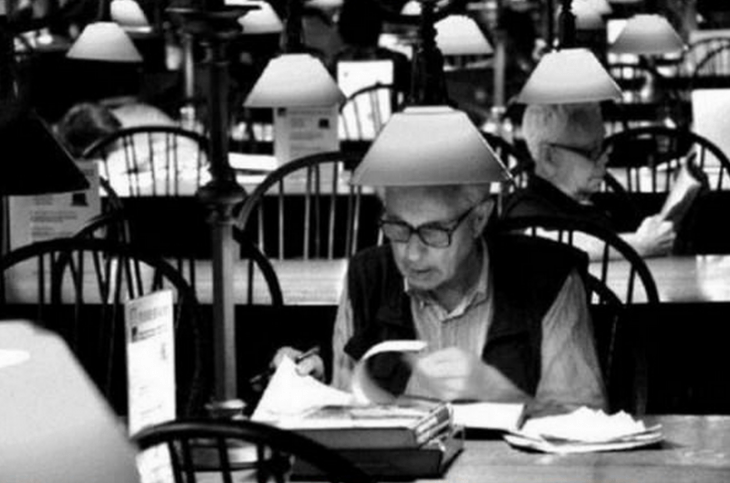 hombre sentado en una mesa leyendo con lampara arriba 