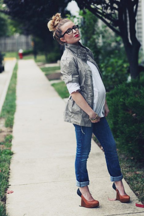 Chica embarazada usando un pantalón de mezclilla, blusa blanca y chaqueta militar 