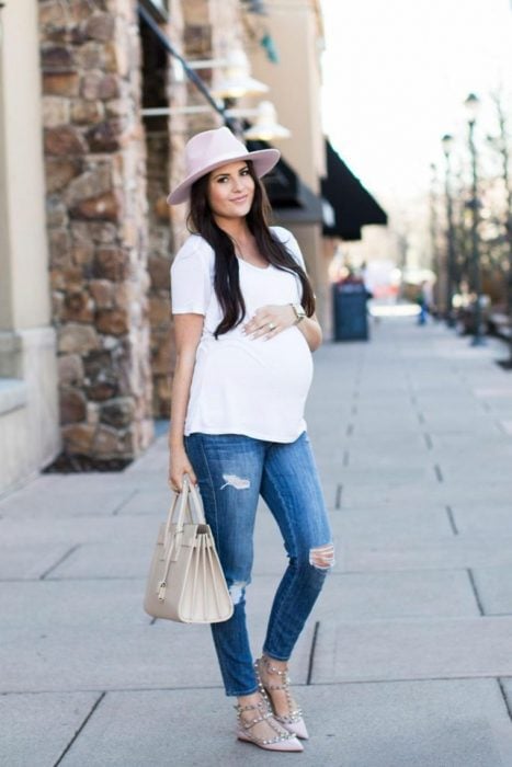 Chica embarazada con sombrero, blusa blanca, pantalón de mezclilla y zapatos color café 