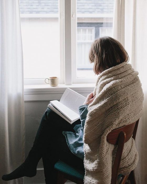 Chica leyendo frente a la ventana con una taza de café 