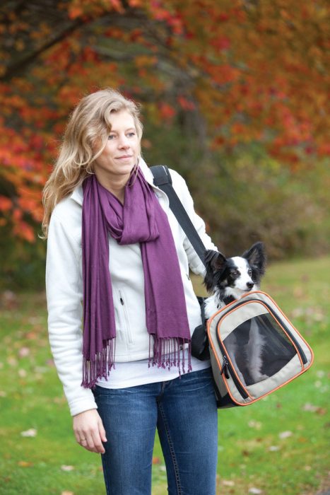 Chica llevando a su perro en una canastilla transportadora