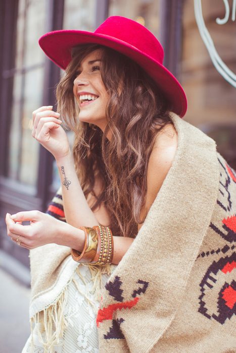 Chica usando un poncho y un sombrero rojo mientras está sentada en unas escaleras 