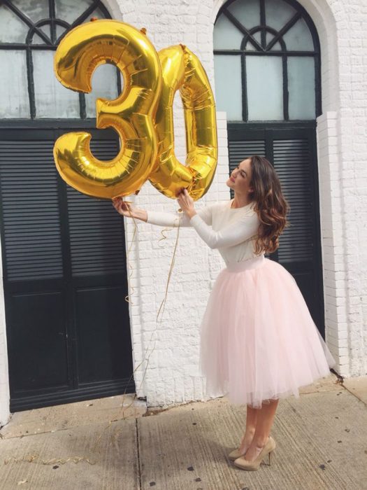 mujer con vestido rosa de tutu cargando globos de numero 30 