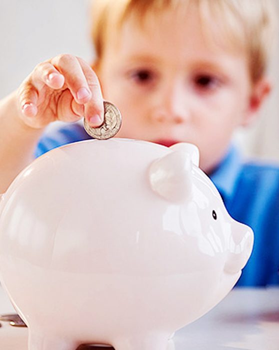 Niño metiendo una moneda en el cochinito. 