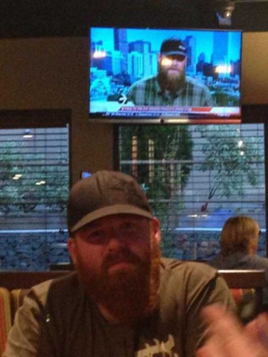 hombre con barba y gorra sentado en un bar y televisión atrás 