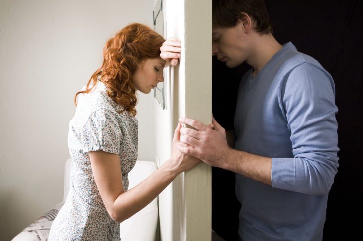 Pareja divididos por un muro, tomándose la mano. 