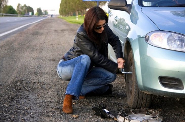 mujer sentada cambiando llanta de coche 