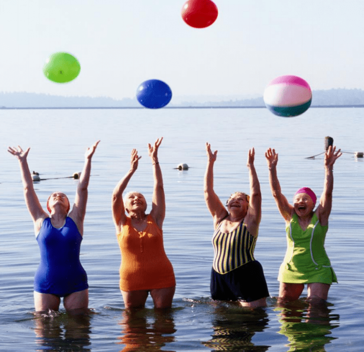 mujeres de 3era edad aventando pelotas en un lago con trajes de baño 