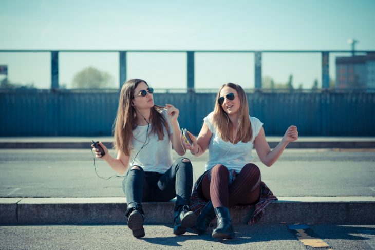 Chicas sentadas en la banqueta escuchando música 