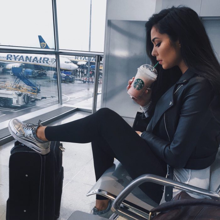 mujer sentada en aeropuerto con maletas y café 