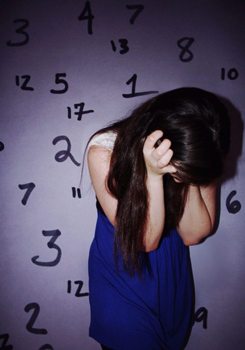 mujer de cabello largo viendo abajo y pared de números 