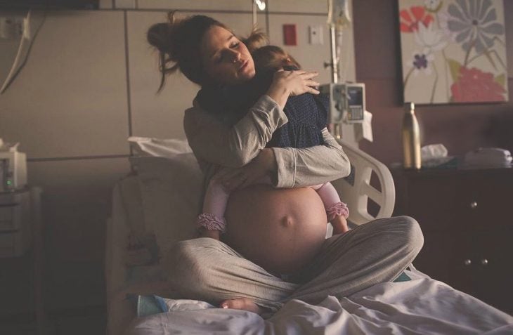 mujer embarazada cargando a niña sobre su vientre 