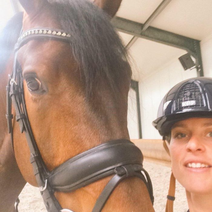 mujer rubia con casco al lado de caballo cafe 