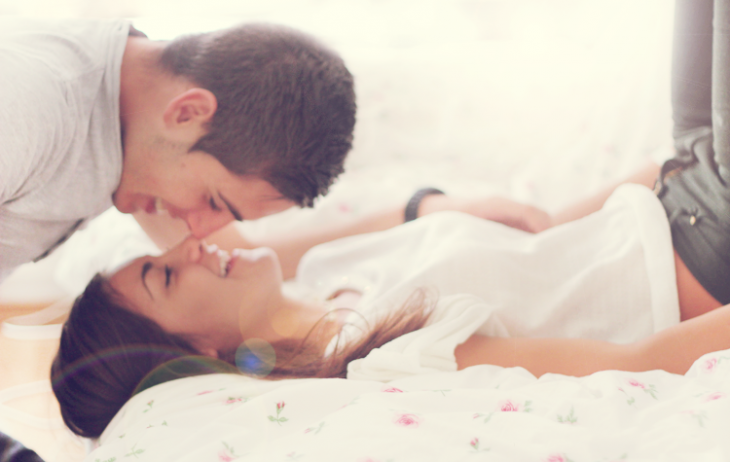Chica recostada en una cama mientras su pareja le da un beso en la nariz 