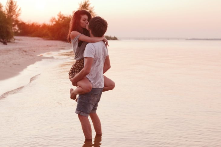 Chico cargando a una chica en brazos mientras están en la playa 